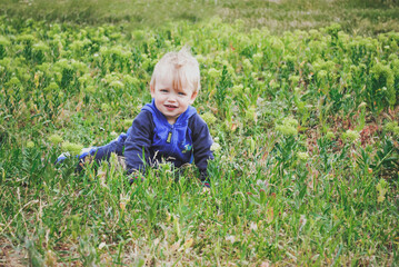 Boy in blue sport suit sitting in the green grass and enjoy cloudy autumn days. Green field and small boy smiling on the camera. Outside games in the grass.