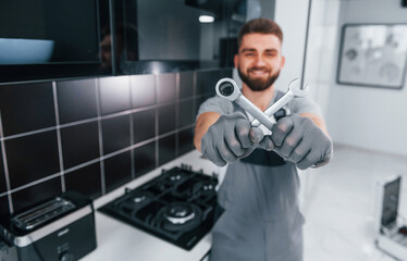 Young professional plumber in grey uniform standing on the kitchen and holding work equipment in...