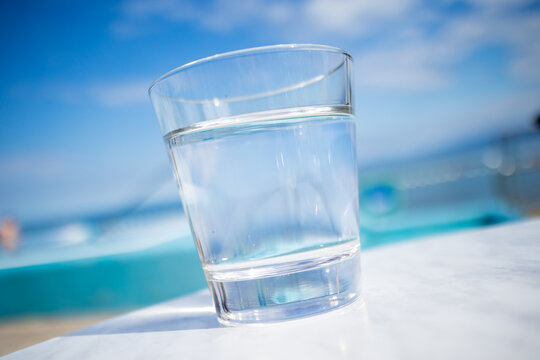 Glass of water standing near swimming pool in hot summer