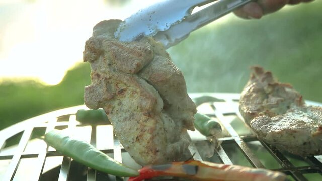 Pieces of steaming grilled pork near chili peppers. a man turns over