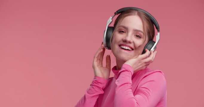 Extremely Happy Girl is dancing on Studio in big Headphones, listening to Music. Amazing satisfied Woman using new Musically Application, wearing stylish modern pink Outfit. Amazing Emotions. Apps.
