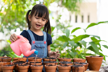 Adorable 3 years old asian little girl is watering the plant  in the pots outside the house,...