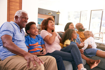 Multi-Generation African American Family Relaxing At Home Sitting On Sofa Watching TV Together