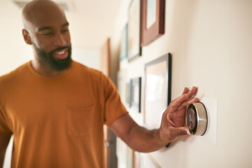 Man Adjusting Digital Central Heating Thermostat At Home - Powered by Adobe