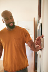 Man Adjusting Digital Central Heating Thermostat At Home