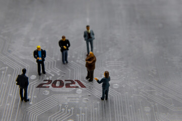 Miniature figurines posed as business people in a meeting over abstract futuristic circuit board...