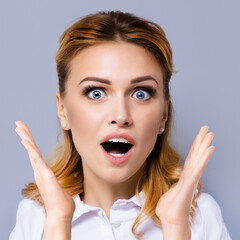 Excited surprised, shocked or very happy amazed business woman with wide opened mouth and eyes, raised up hands. Face portrait studio image, square composition.