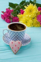 Cup of coffee flowers bouquet and love symbol. Blue wooden background.