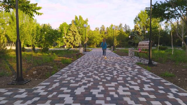 Lonely child running on empty square near closed playground because of the quarantine. A girl with long blonde braid playing alone near fenced showground without children. Lockdown social distance.