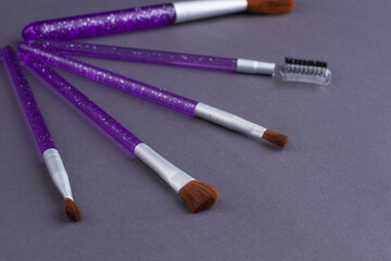 Close up different layout brushes with purple handle. Cosmetic skincare brushes on a smooth grey surface.