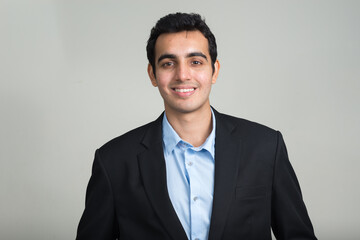 Portrait of happy young handsome Indian businessman in suit smiling