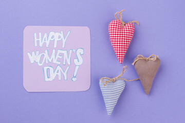 Flat lay colored soft textile hearts. Happy women's day wish. Isolated on purple background.