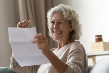 Elderly woman sit on couch at home read letter feels excited by great news in notification, bank...