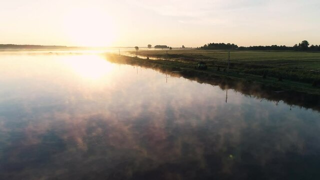 Aerial drone shot of rising sun in the morning. Morning mist floating above the lake. Morning fog on the pond, sunrise shot. Golden rays of the sun paint the fog over the pond. Fishing holiday concept