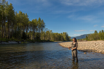An asian women in waders, fishing a river in British Columbia, Canada