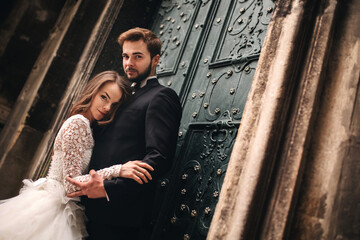 Wedding couple hugs near the vintage green door. Stone walls in ancient town background. bride with...