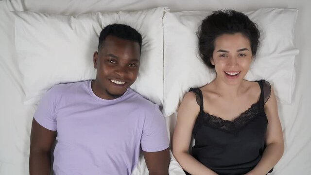 Mixed-race couple lying in bed and making fist bump gesture. Top view. Friendship concept
