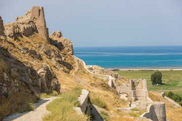 Panoramic view of Van Castle and Lake Van. Clay towers, stone walls on the background of blue sky and turquoise water of the lake. Beautiful places and sights of Eastern Turkey