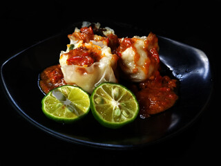 fish dumplings with peanut sauce and sliced ​​lime on a black plate with a black background