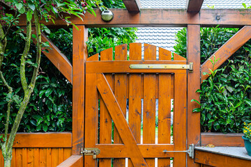 Wooden gate and fence on the back of the home garden. The gate is closed with a padlock.