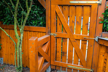 Wooden gate and fence on the back of the home garden. The gate is closed with a padlock.