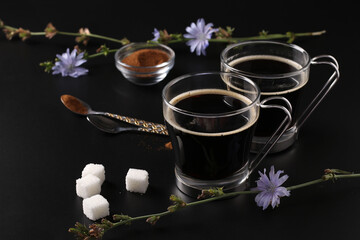 Obraz na płótnie Canvas Chicory beverage in two glass cups, with concentrate and flowers on black background. Healthy herbal beverage, coffee substitute, Closeup