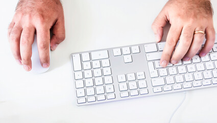 male hand clicking on a mouse and typing on a white keyboard on a white table