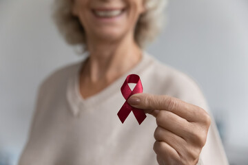Close up aged female show to camera red ribbon symbol, substance-abuse prevention, solidarity of people living with HIV awareness fight against AIDS. World AIDS Day. Health check up promotion concept - obrazy, fototapety, plakaty