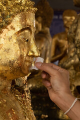 Buddhist believer attaching a gold leaf at the mouth of Buddha statue