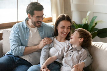 Emotional young couple enjoying spending free weekend time with small preschool child son. Happy small boy laughing at funny joke, having fun communicating with loving parents in living room.