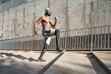 Athletic black man is training in urban area while wearing a mask.