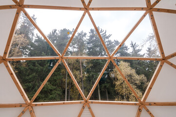 Interior of large geodesic wooden dome tent with window and view to forest. Empty interior glamping...
