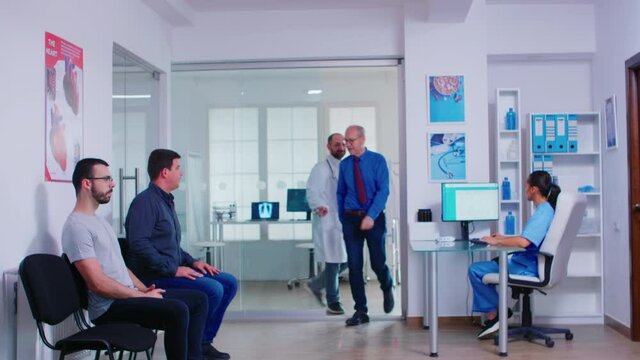 Medic talking with disabled woman in hospital waiting area while inviting patient in examination room. Young man waiting for doctor consultation. Health care system and medicine staff