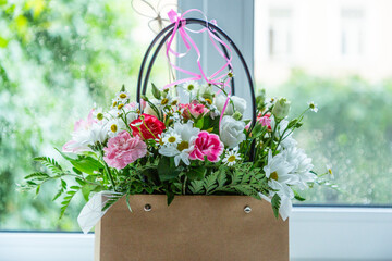 A bouquet of white and pink summer flowers standing in a woman's bag on the window. Daylight falls from the window.  Decorative concept of blooming with flowers. The background is blurred.