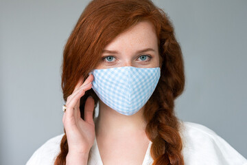 Woman wearing stylish diy protective face mask, posing on blue background. Trendy Fashion accessory during quarantine of coronavirus pandemic. Close up studio portrait. Copy, empty space for text