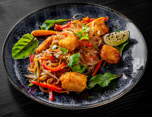 Tasty asian noodles with fried cheese tofu and vegetables in plate on black wooden table background