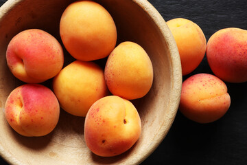 Fototapeta na wymiar Photography of apricots in a wooden bowl, on slate background for food illustrations