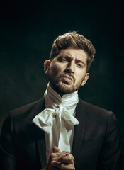 Sincere sin. Young man in suit as Dorian Gray isolated on dark green background. Retro style,...