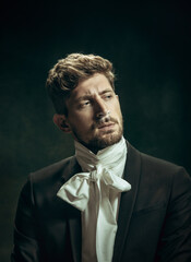 Sincere sin. Young man in suit as Dorian Gray isolated on dark green background. Retro style, comparison of eras concept. Beautiful male model like classic literature character, old-fashioned.