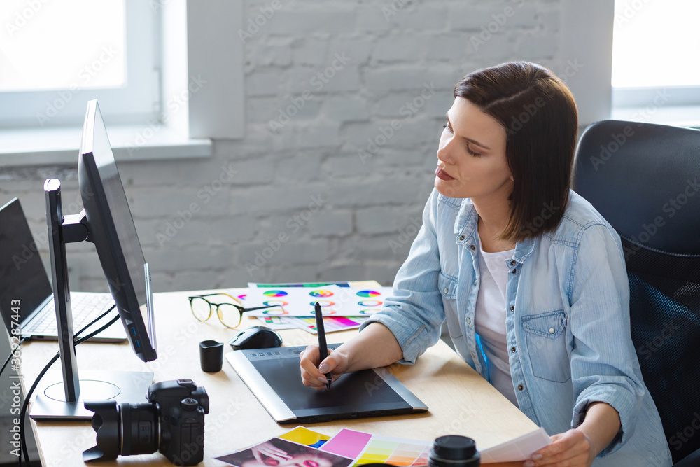 Poster Portrait of graphic designer working in office with laptop,monitor,graphic drawing tablet and color palette.Retouching images in special program.Retoucher workplace in photo studio.Creative agency.