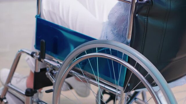 Disabled old woman holding hands on chair wheell in hospital hallway. Disabled disability handicapped impairment disease treatment and patient paralysis