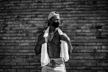 Athletic black man is training in front of the grey wall while wearing a mask. Black and white photo.