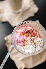 ice cream white and pink in a transparent cream bowl on a black table against the background of coffee