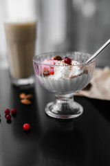 ice cream white and pink in a transparent cream bowl with nuts and berries on a black table