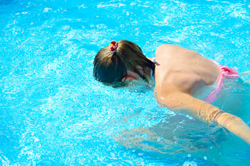 the girl is in the water in the pool, lowered her head into the water, learns to dive