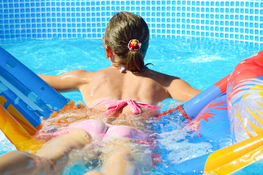 girl in a pink swimsuit swims in the pool on a bright inflatable mattress, lying on it on her stomach