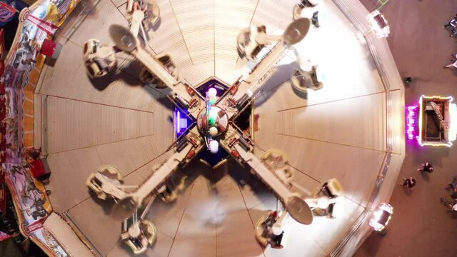 Aerial shot of scrambler or twister ride in amusement park with flashing strobe lights. Drone shot.
