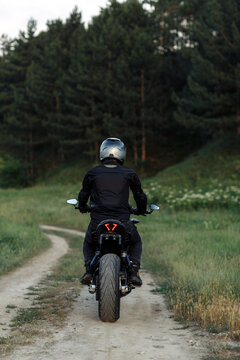 Back view of biker driving motorcycle in sunset on the country road.