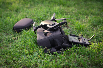 black camera drone with remote controller and phone as a screen stays on the green grass, technology concept