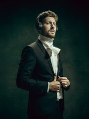Music listening. Young man in suit as Dorian Gray isolated on dark green background. Retro style,...